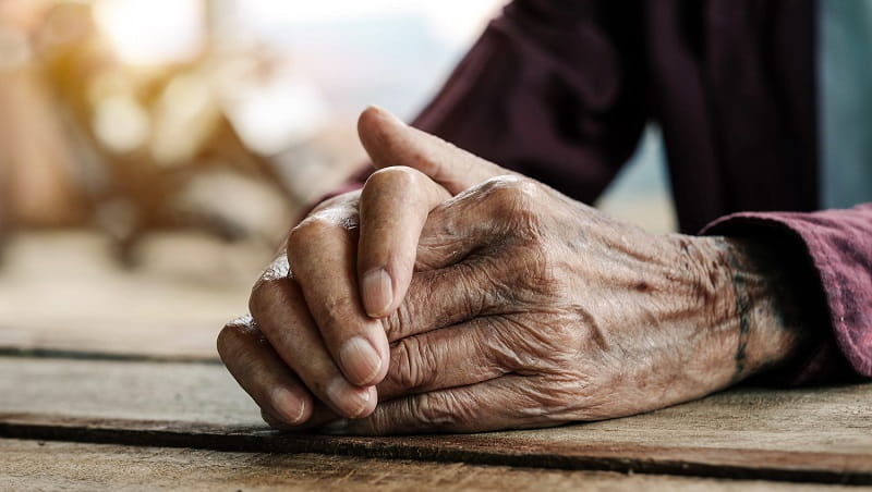 An old man's hands resting on a wooden bench.